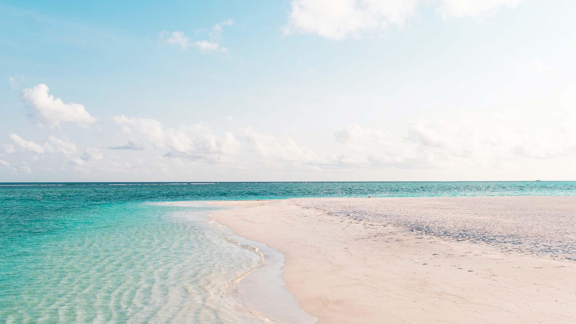 Weißer Sandstrand mit türkisblauem Meer und leicht bewölktem Himmel an der Küste