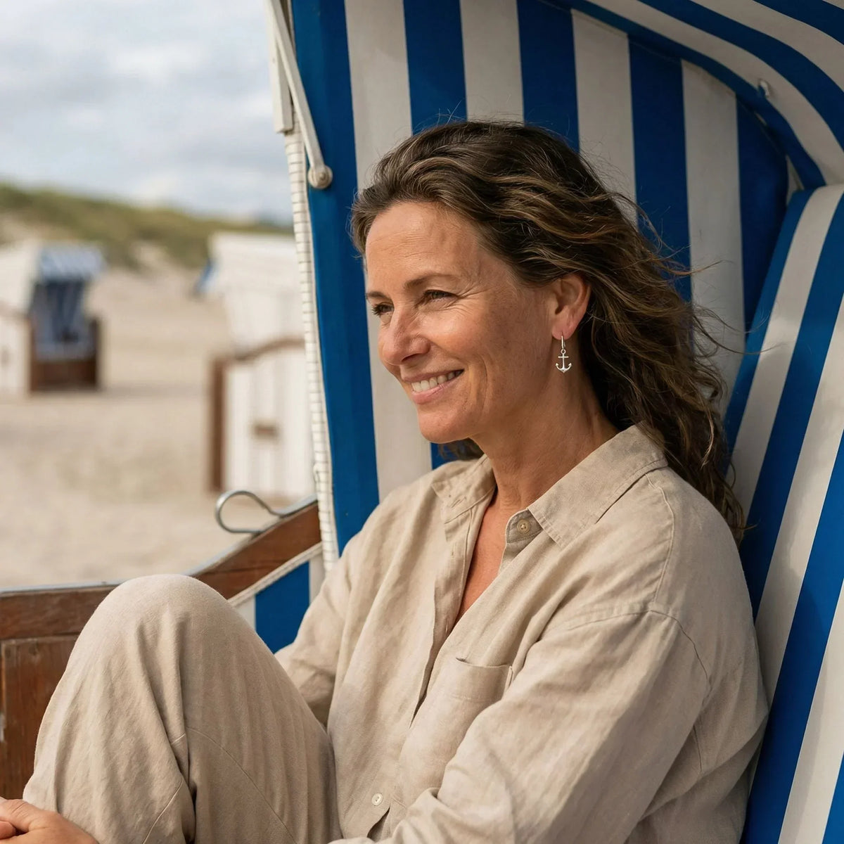 Frau am Strand im Strandkorb, trägt silbernen Anker-Ohrring, maritimer Schmuck