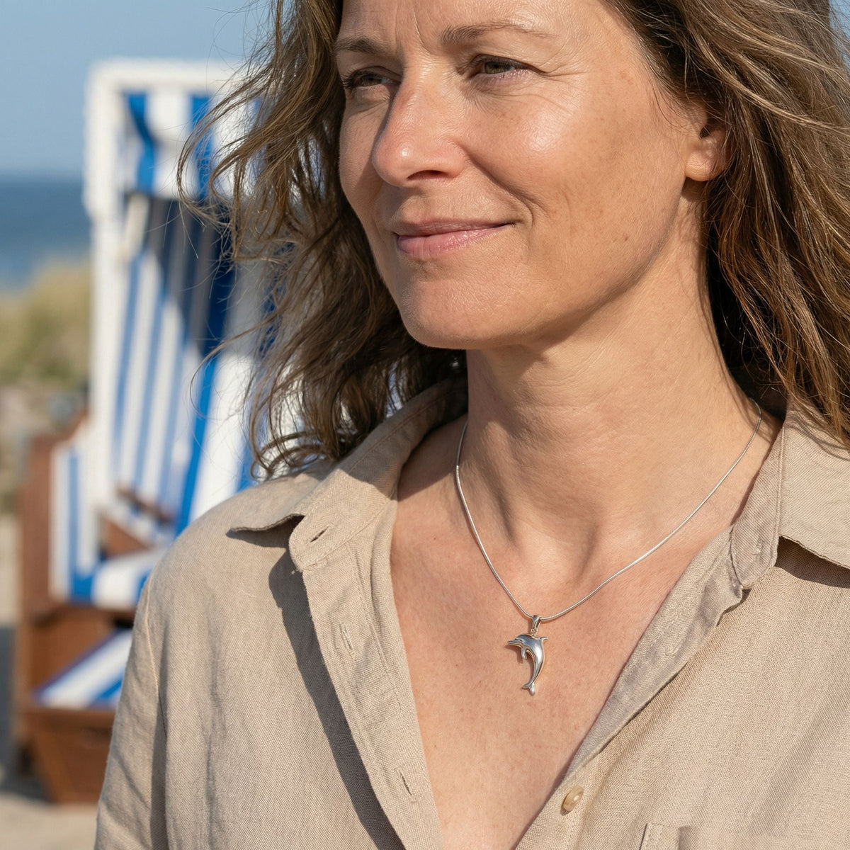 Frau mit silberner Delfin-Kette am Strand, maritimer Schmuck, Sommermode