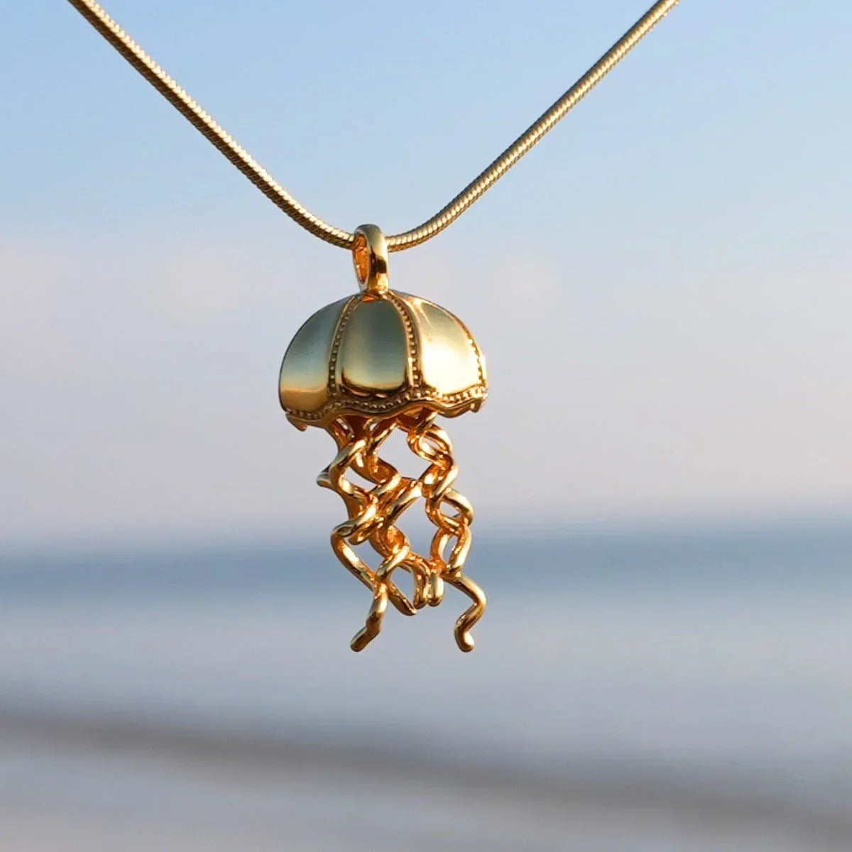 Goldene Qualle Anhänger Kette maritimer Schmuck vor unscharfem Strand Hintergrund