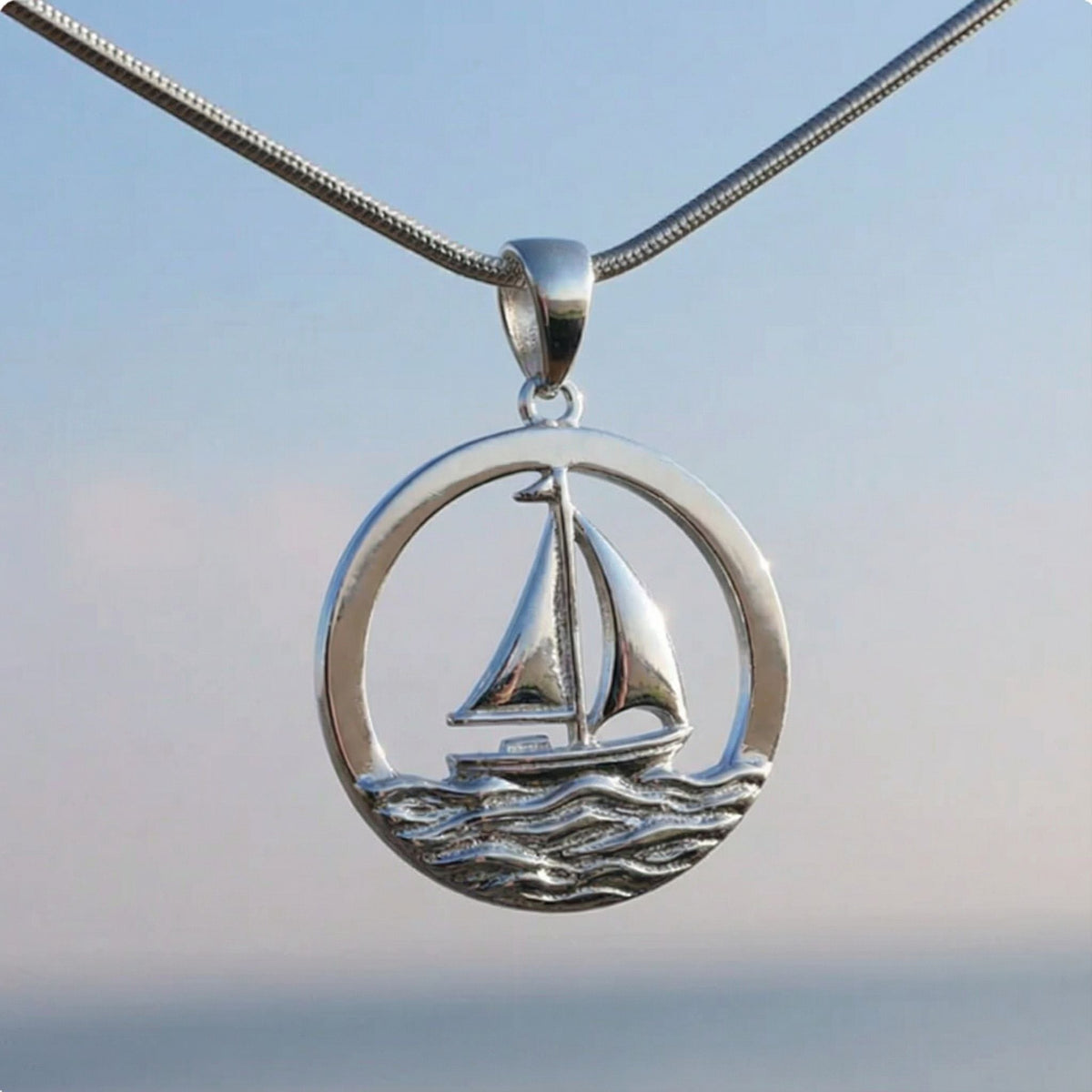 Silberner Segelschiff-Anhänger mit maritimen Wellenmotiv vor blauem Himmel