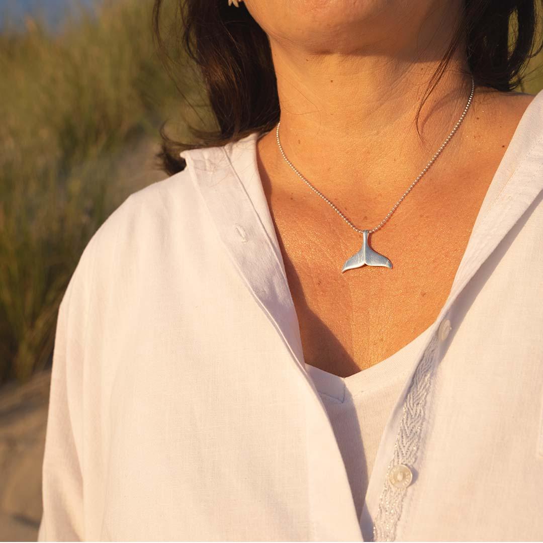 Frau mit silberner Walflossen-Kette am Strand, maritimer Schmuck in Nahaufnahme