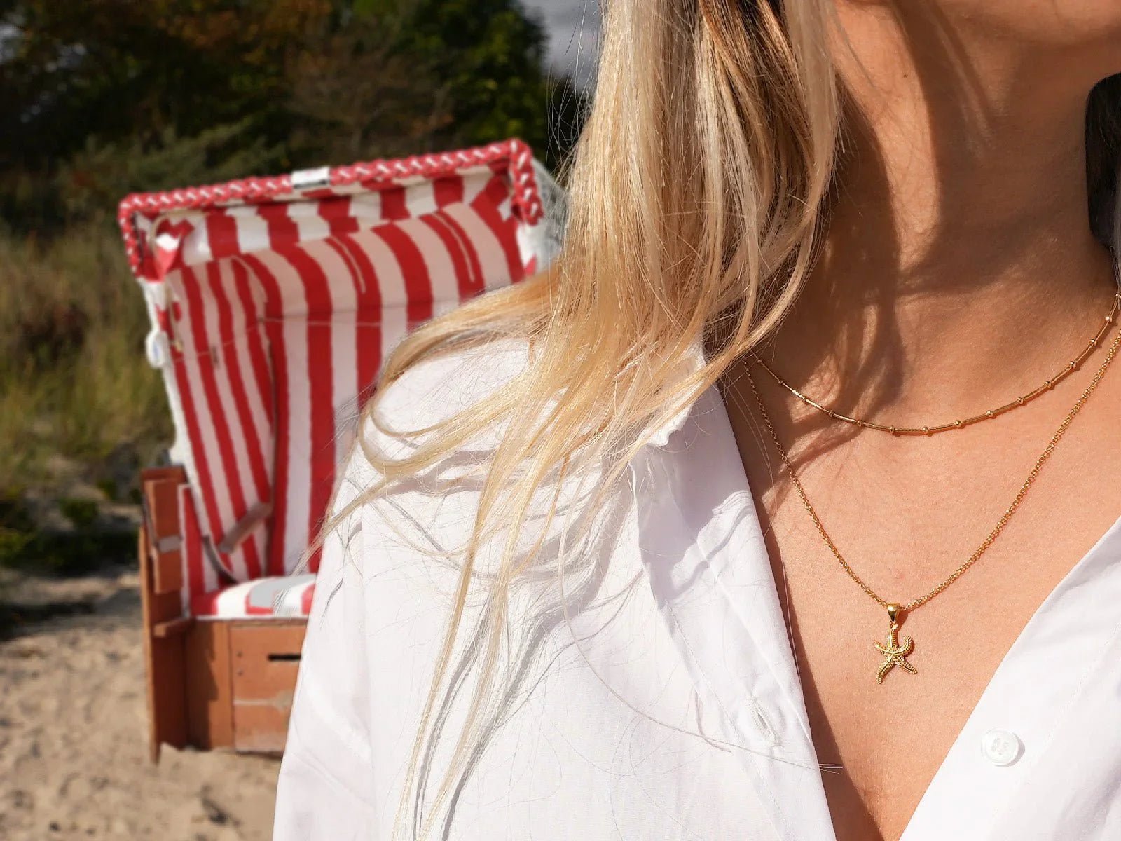 Frau mit 18k vergoldeter Sternanhänger-Kette am Strand vor Strandkorb
