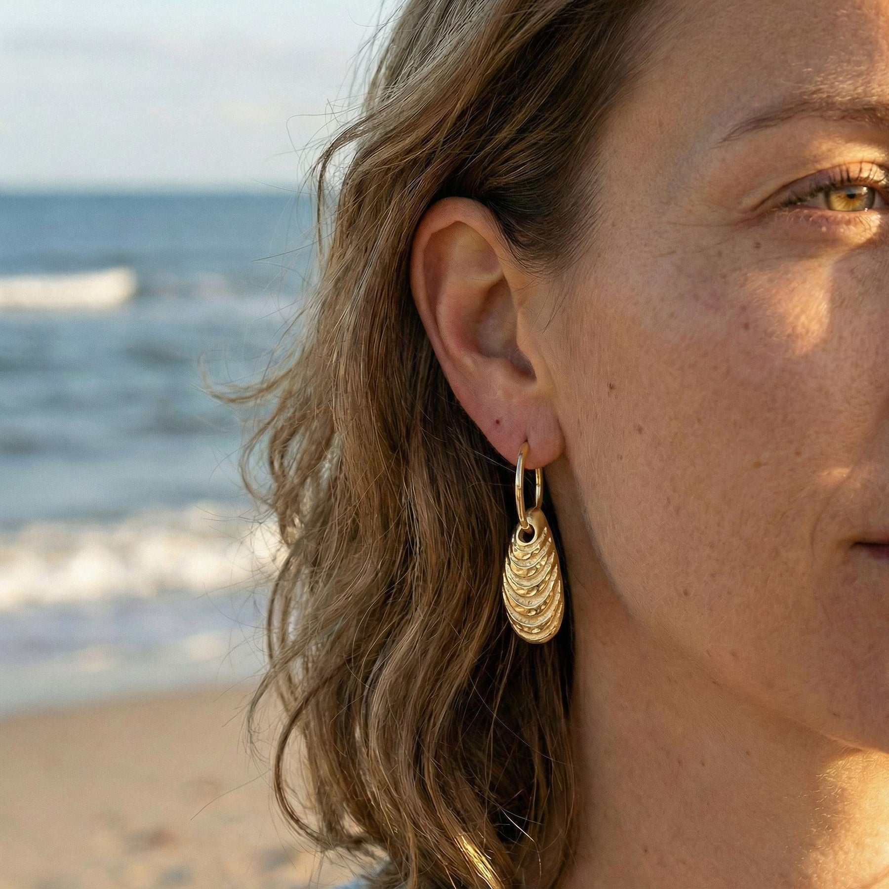 Goldener Miesmuschel-Anhänger am Creolen-Ohrring, maritimer Schmuck am Strand getragen