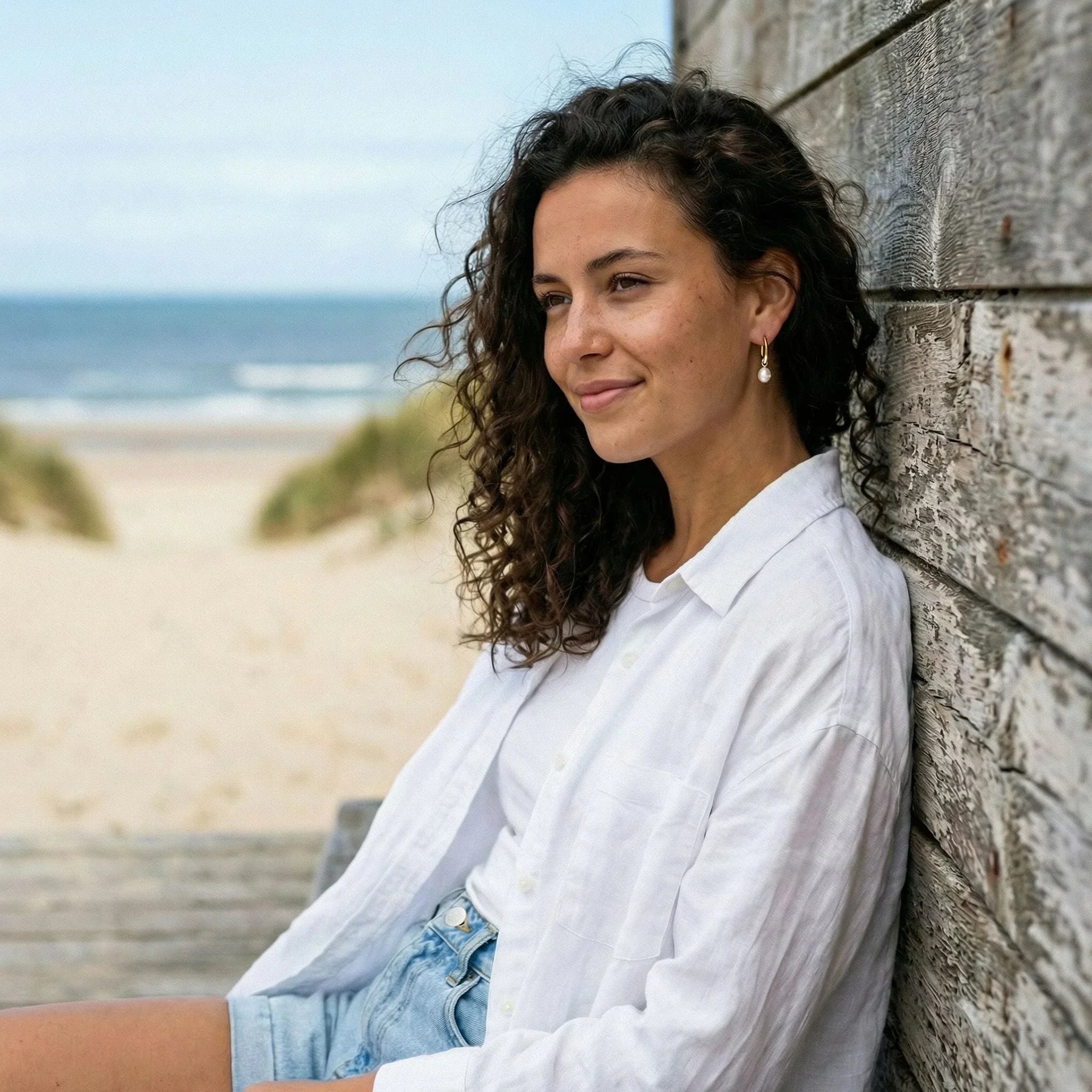 Frau mit goldenen Creolen-Ohrringen und Perlenanhänger am Strand, Sommermode, maritimer Schmuck