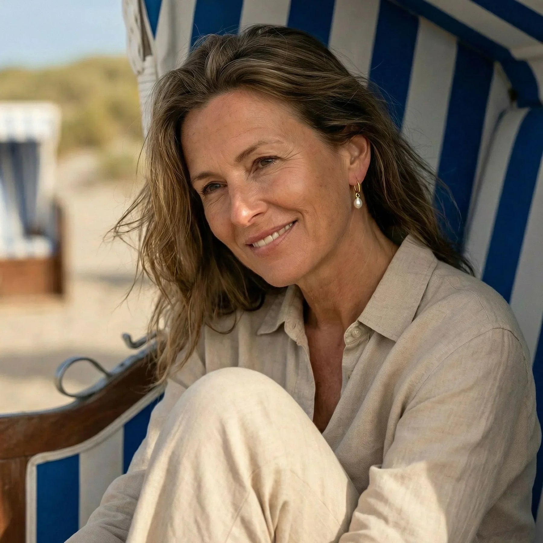 Frau am Strand mit goldfarbenem Creolen-Ohrring und Perlenanhänger, maritimer Schmuck