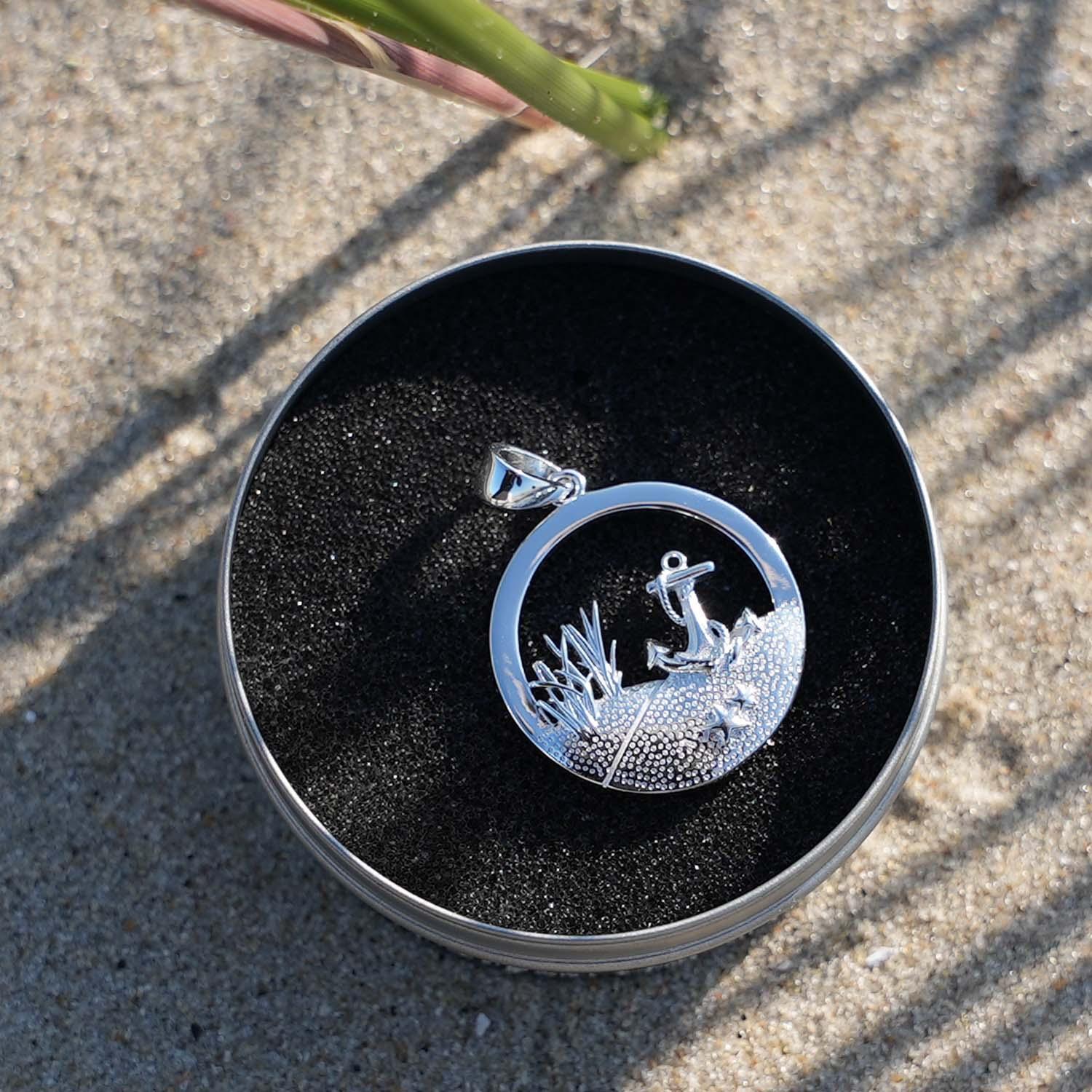 Runder Silberanhänger mit Anker-Motiv und Dünen im maritimen Stil, auf Sand präsentiert.