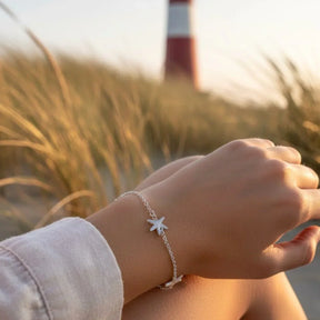 Silber Armband mit Seestern-Anhängern am Handgelenk, maritimes Motiv, Leuchtturm im Hintergrund
