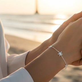 Silbernes Armband mit Seestern-Motiven am Handgelenk, maritimer Schmuck am Strand
