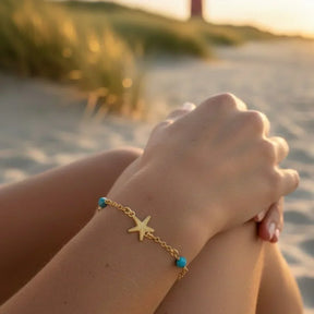 Goldenes Armband mit Seestern und blauen Perlen am Handgelenk am Strand