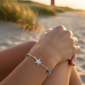 Silbernes Armband mit Seestern-Anhänger und blauen Perlen am Strand im Sonnenuntergang