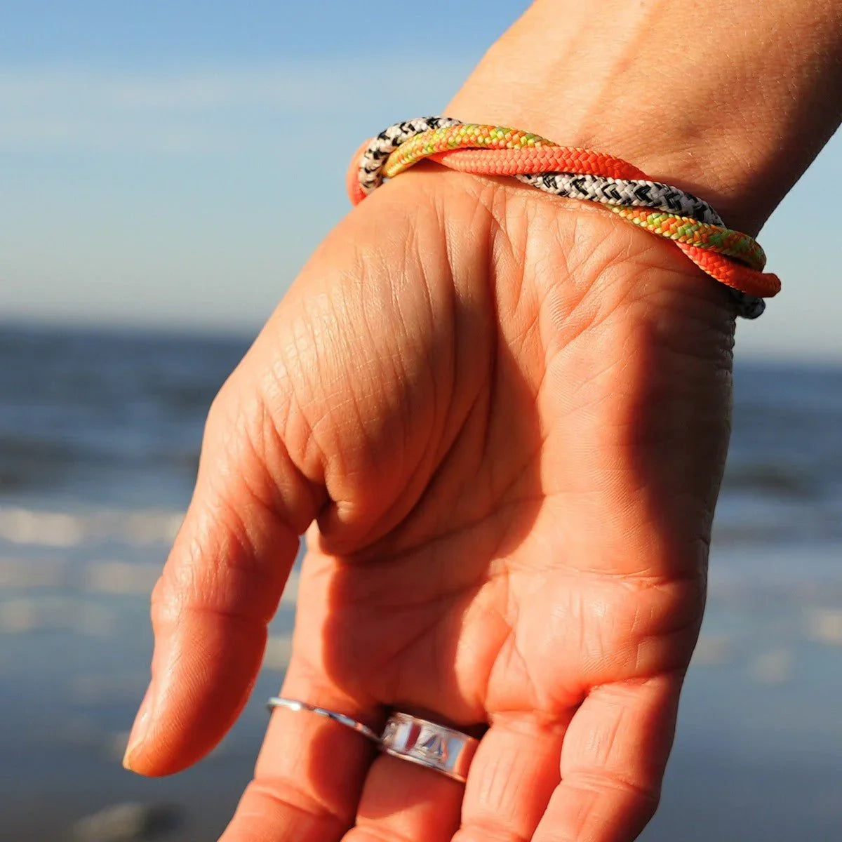 Maritimes Armband aus bunt geflochtenem Seil am Handgelenk am Strand vor dem Meer