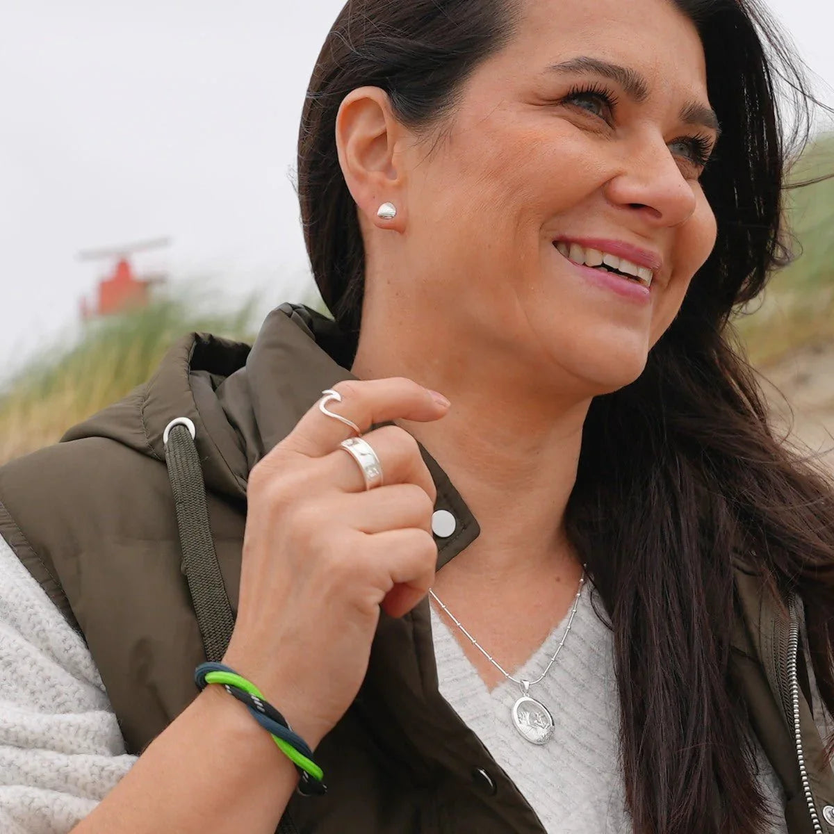 Frau mit grün-blauem Armband, maritimem Schmuck und Dünen im Hintergrund