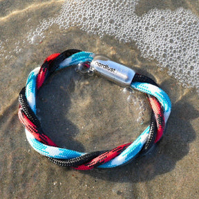 Maritimes Armband im Watt mit blau, rot, schwarz und weiß geflochtenem Band am Strand
