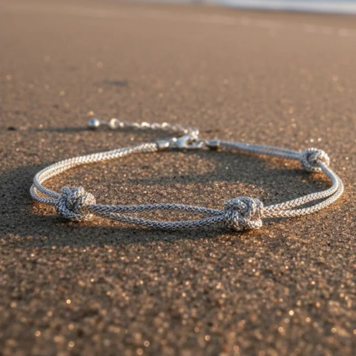 Silbernes Armband mit drei Wellenknoten auf Sand am Strand, maritimer Schmuck