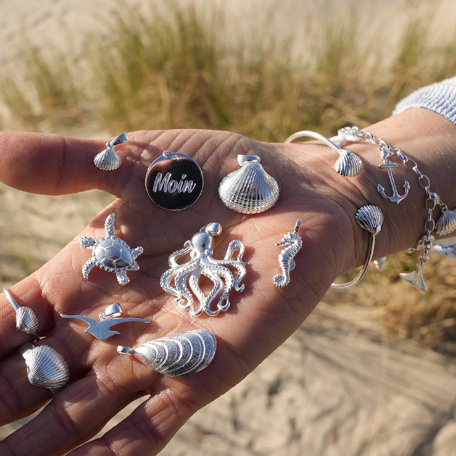 Silberner Armreif und maritimer Schmuck mit Muschel, Seestern, Anker und Seepferdchen am Strand