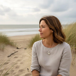Frau am Strand mit maritane Kette mit silbernem Deichschaf-Anhänger, Dünen und Meer