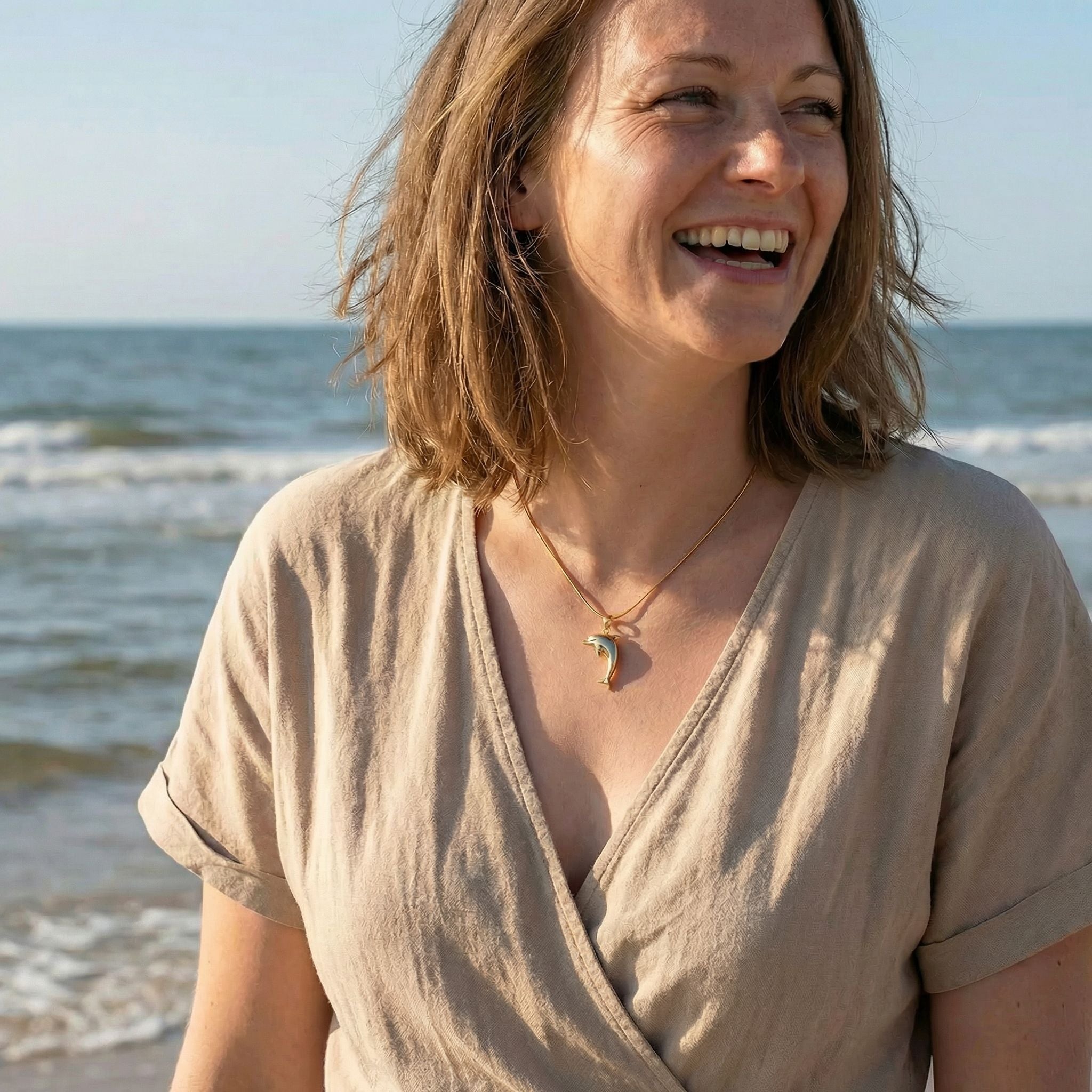 Frau am Strand mit goldener Delfin-Kette, maritimer Schmuck, sommerliches Outfit