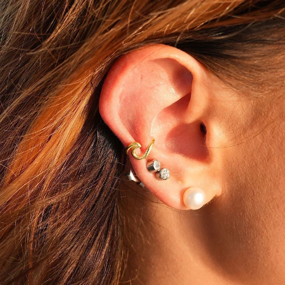 Goldener Ear Cuff in Wellenform am Ohr, maritimer Schmuck Trend, kombiniert mit weiteren Ohrringen