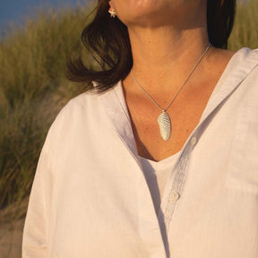 Frau mit silberner Muschel-Anhänger Kette am Strand, maritimer Schmuck im Sonnenlicht