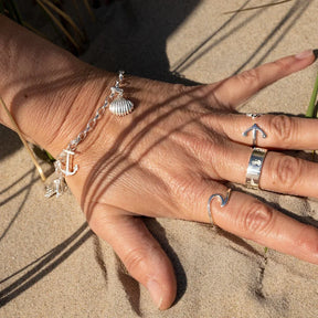 Silbernes Armband mit Herzmuschel- und Ankeranhänger am Handgelenk im Sand am Strand