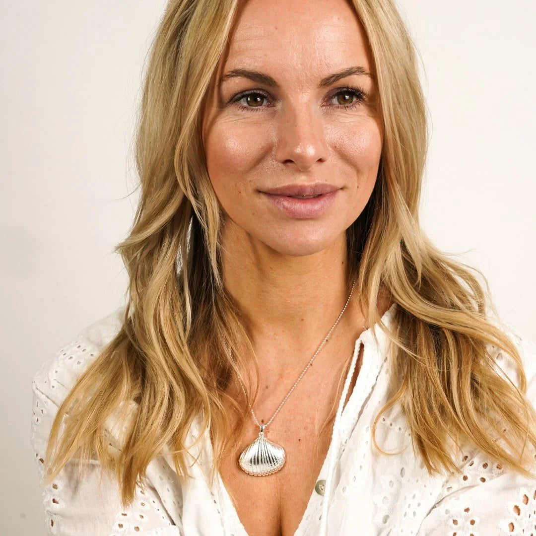 Frau mit langer Kette mit silbernem Herzmuschel-Anhänger, maritimer Schmuck, weißes Oberteil