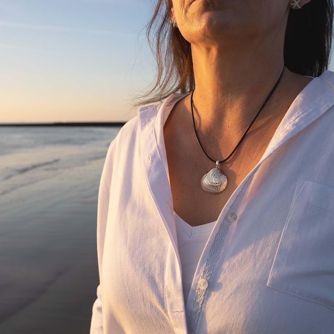 Frau am Strand mit Herzmuschel-Anhänger aus Silber an schwarzem Band, maritime Schmuckkette