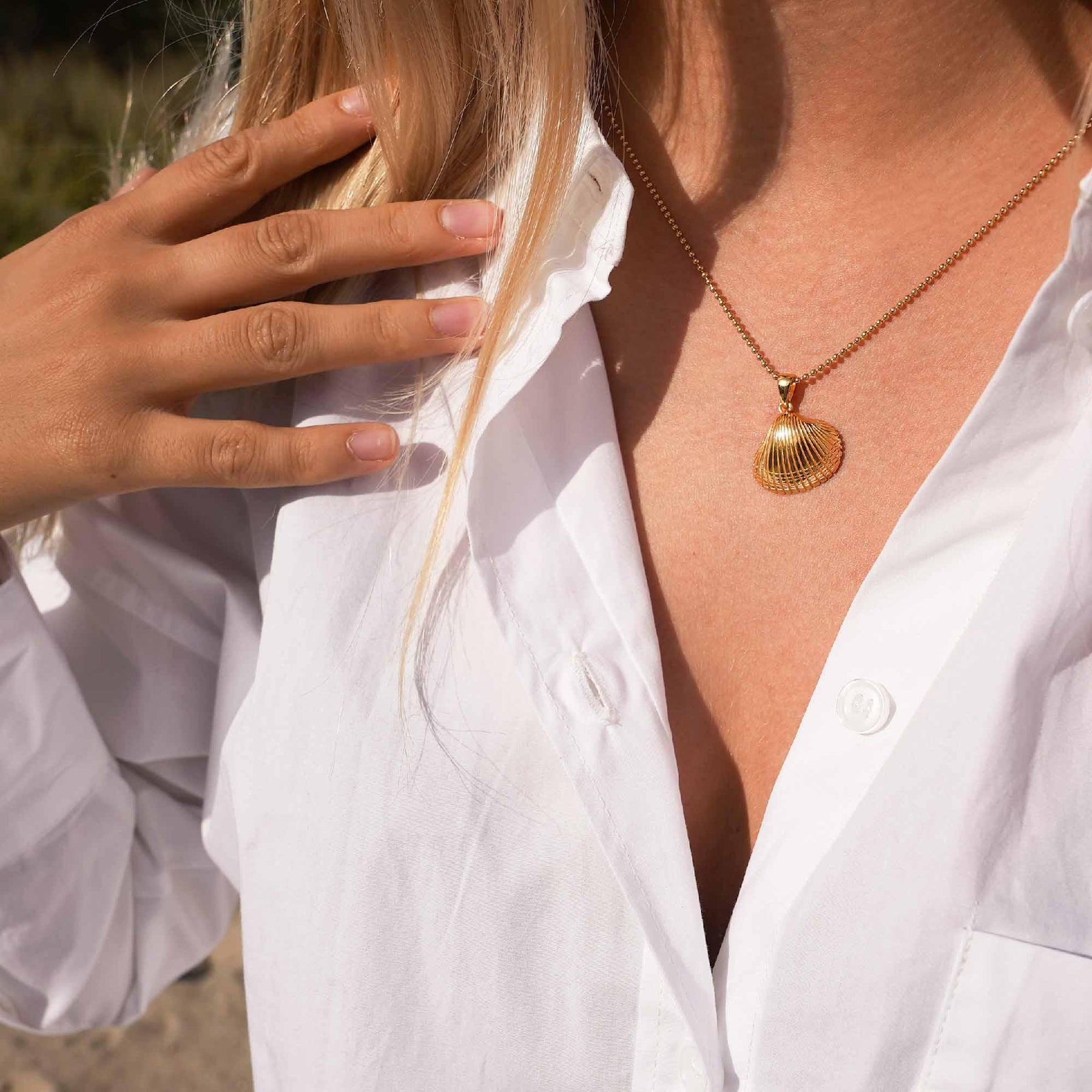 Goldene Muschel-Kette an Frau mit weißer Bluse, maritimer Schmuck, Nahaufnahme