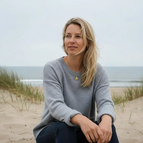 Frau am Strand mit goldener Herzmuschel-Kette, maritimer Schmuck, Dünen und Meer im Hintergrund
