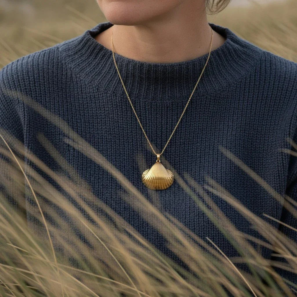 Frau mit goldener Herzmuschel-Kette im maritimen Stil vor Dünenlandschaft