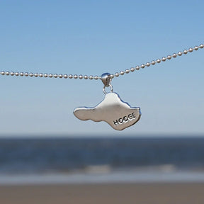 Silberne Halskette mit Insel Hooge Anhänger vor Meer und blauem Himmel