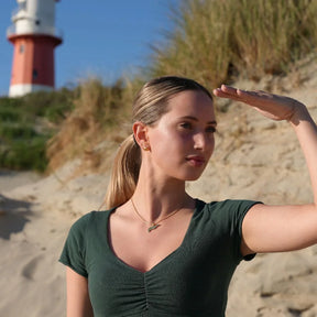 Junge Frau mit maritimem Schmuck steht am Strand vor Leuchtturm auf Spiekeroog
