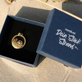 Goldener Anhänger mit Krebs-Motiv in Schmuckbox, maritimer Schmuck auf Sand