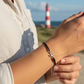 Schwarzes Lederarmband mit silbernem Anker, maritimer Schmuck am Handgelenk vor Leuchtturm