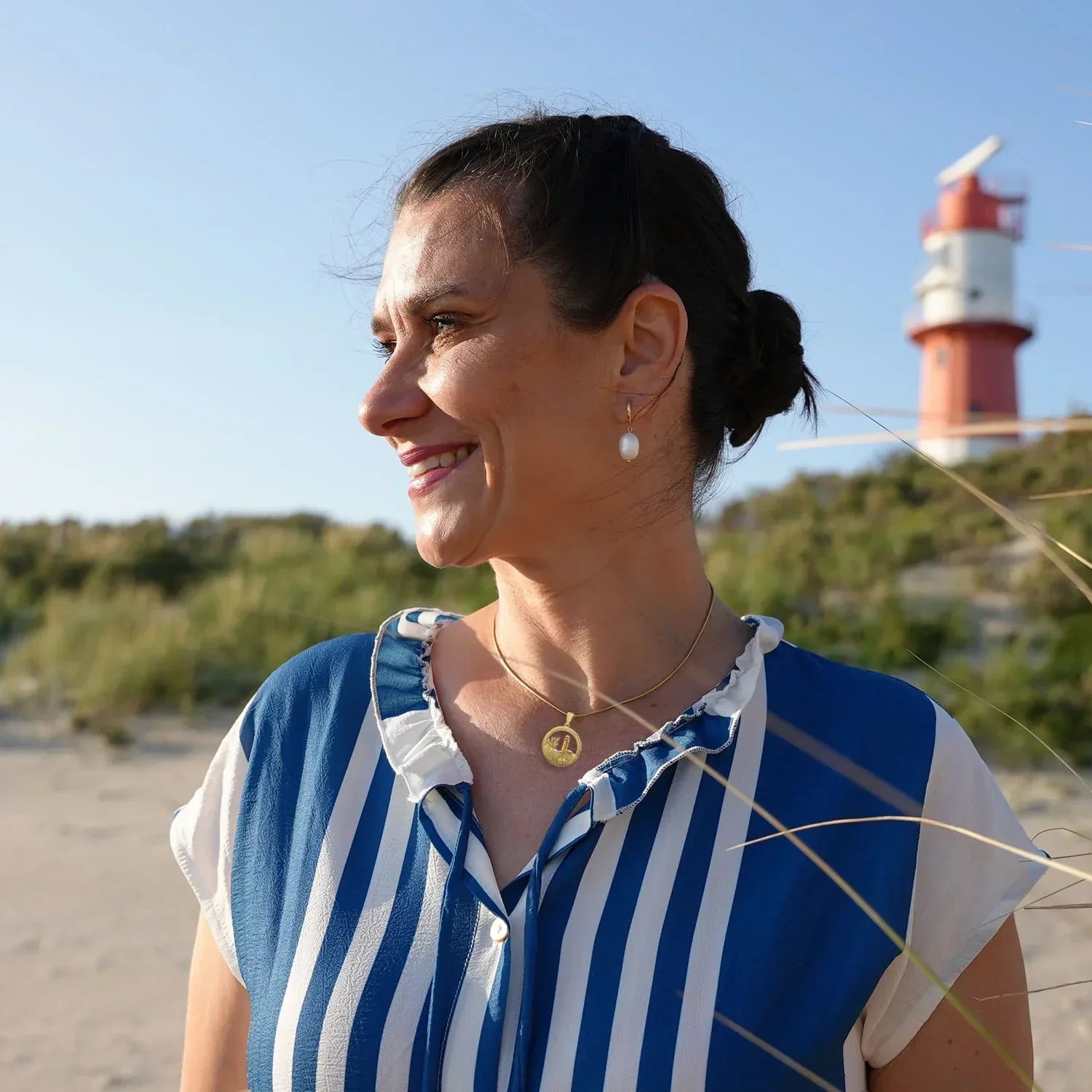 Frau am Strand mit goldener Anhängerkette, maritimer Schmuck, Leuchtturm im Hintergrund