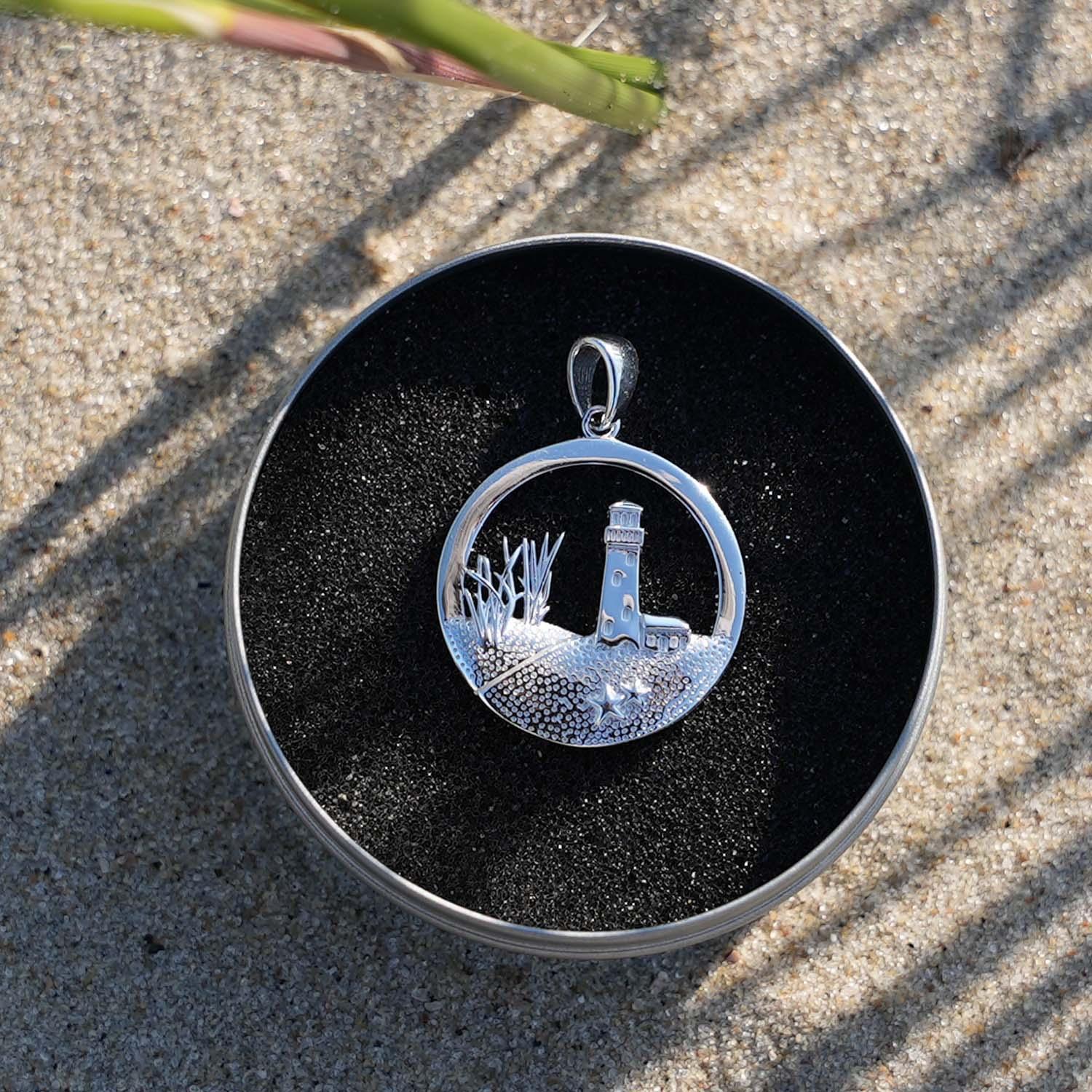 Silberner runder Anhänger mit Leuchtturm-Motiv, maritimer Schmuck am Strand fotografiert