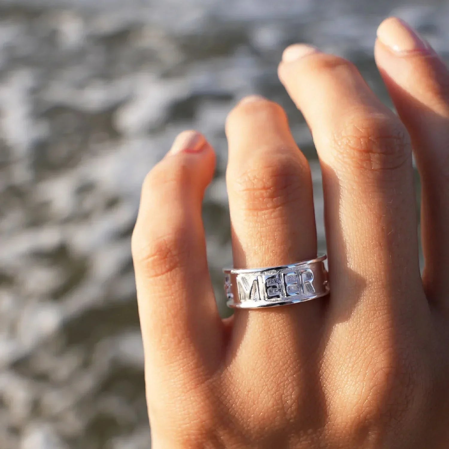 Silberring mit Gravur 'MEER' am Finger, maritimer Schmuck am Strand mit Meereswellen