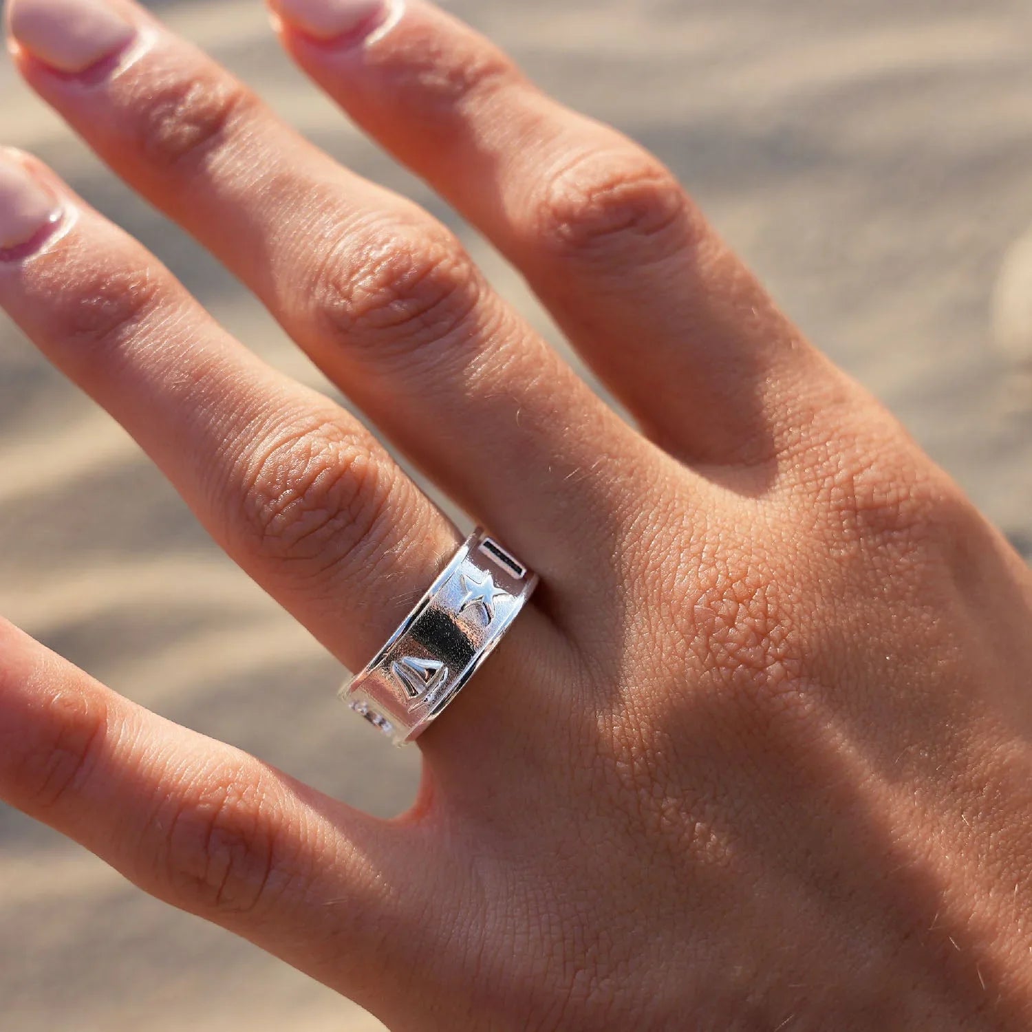 Silberner Ring mit maritimen Motiven am Finger vor sandigem Hintergrund