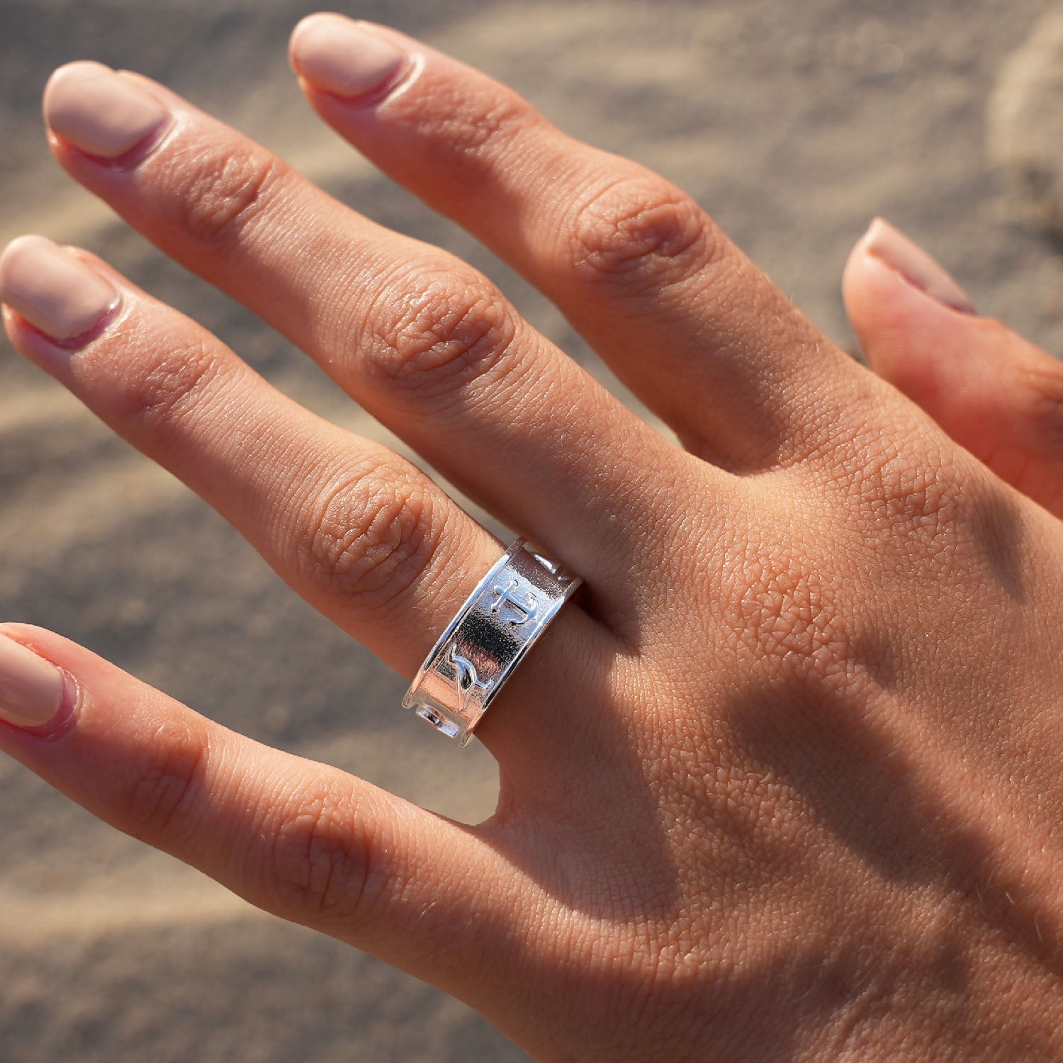 Silberner maritimer Ring mit Wellenmuster an Hand am Strand