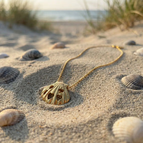 Goldene Muschel-Kette mit Herzmotiven im Sand am Strand, maritimer Schmuck