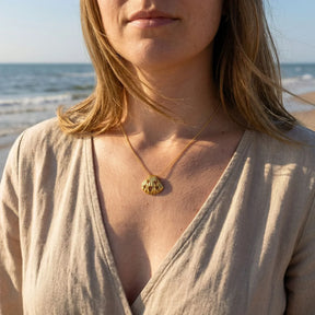Frau trägt goldene Muschel-Kette mit Herzmotiv am Strand, maritimer Schmuck