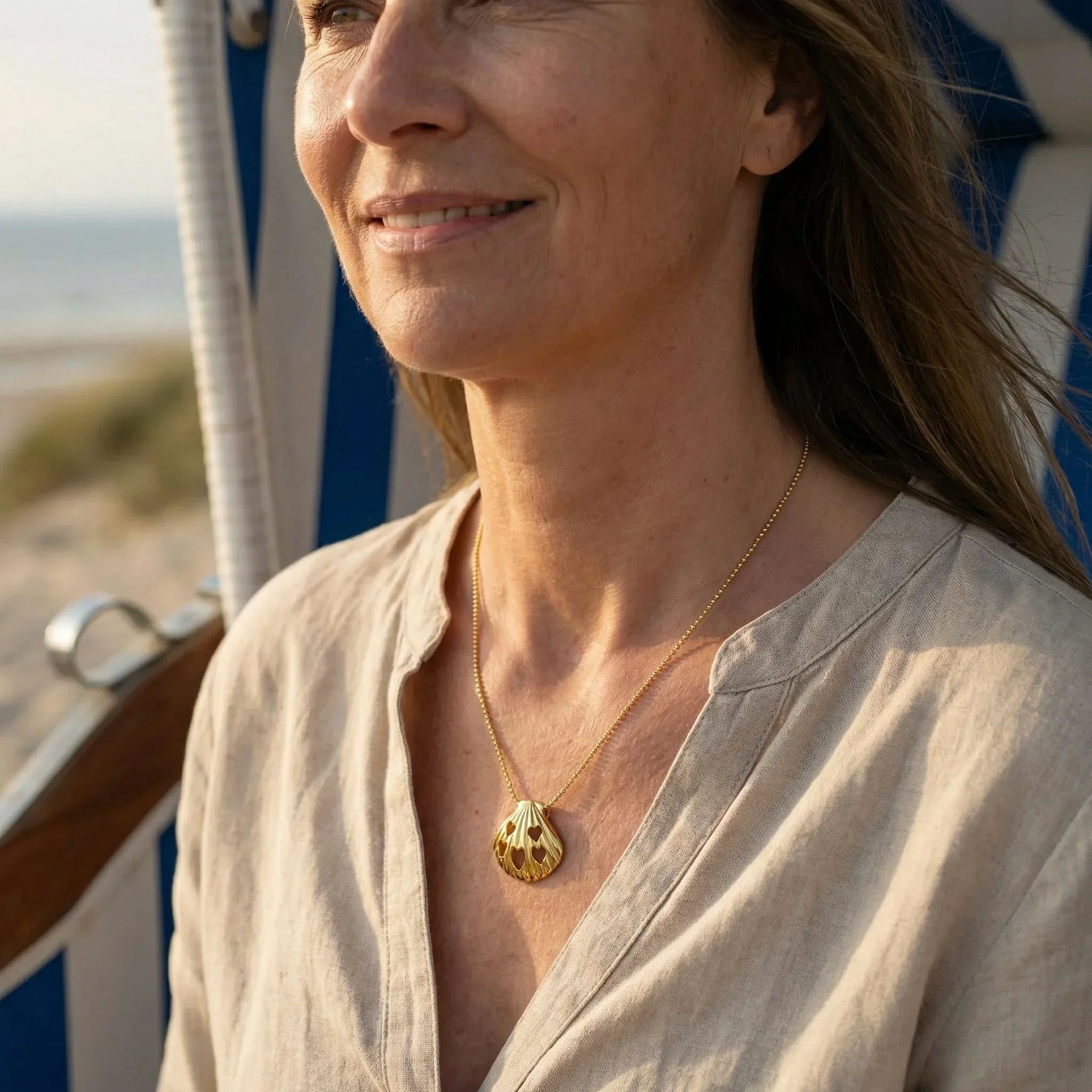 Frau am Strand mit goldener Muschel-Halskette, maritime Schmuckkette mit Herz-Motiven