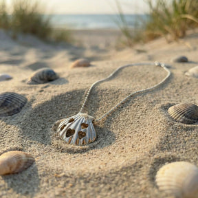 Silberne Muschel-Halskette mit Herzmotiven im Sand am Strand, umgeben von Muscheln