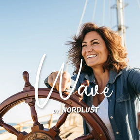 Lächelnde Frau am Schiffssteuer bei Sonnenschein, maritimes Flair, Schriftzug Wave by Nordlust sichtbar