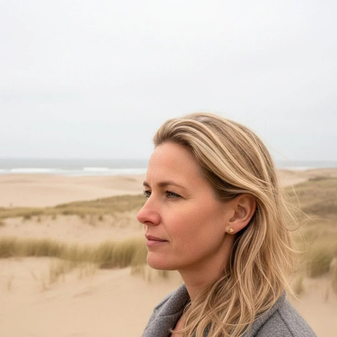 Frau am Strand mit goldenen Knoten-Ohrsteckern, maritimer Schmuck, Dünen im Hintergrund