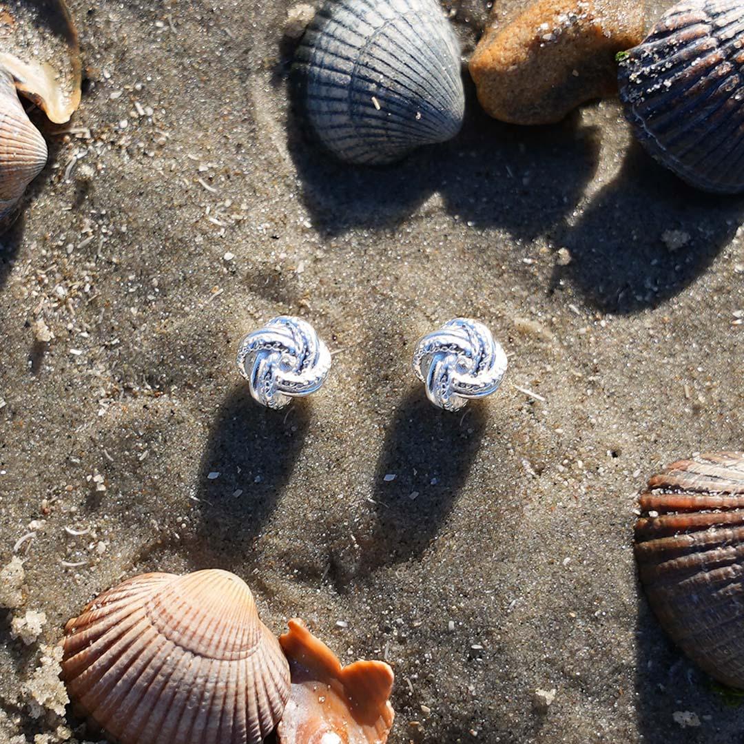 Ohrstecker Knoten silber auf Sand mit Muscheln, maritimer Schmuck am Strand