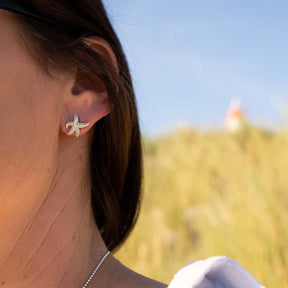 Silberner Seestern Ohrstecker am Ohr einer Frau, maritimer Schmuck, draußen im Sonnenschein