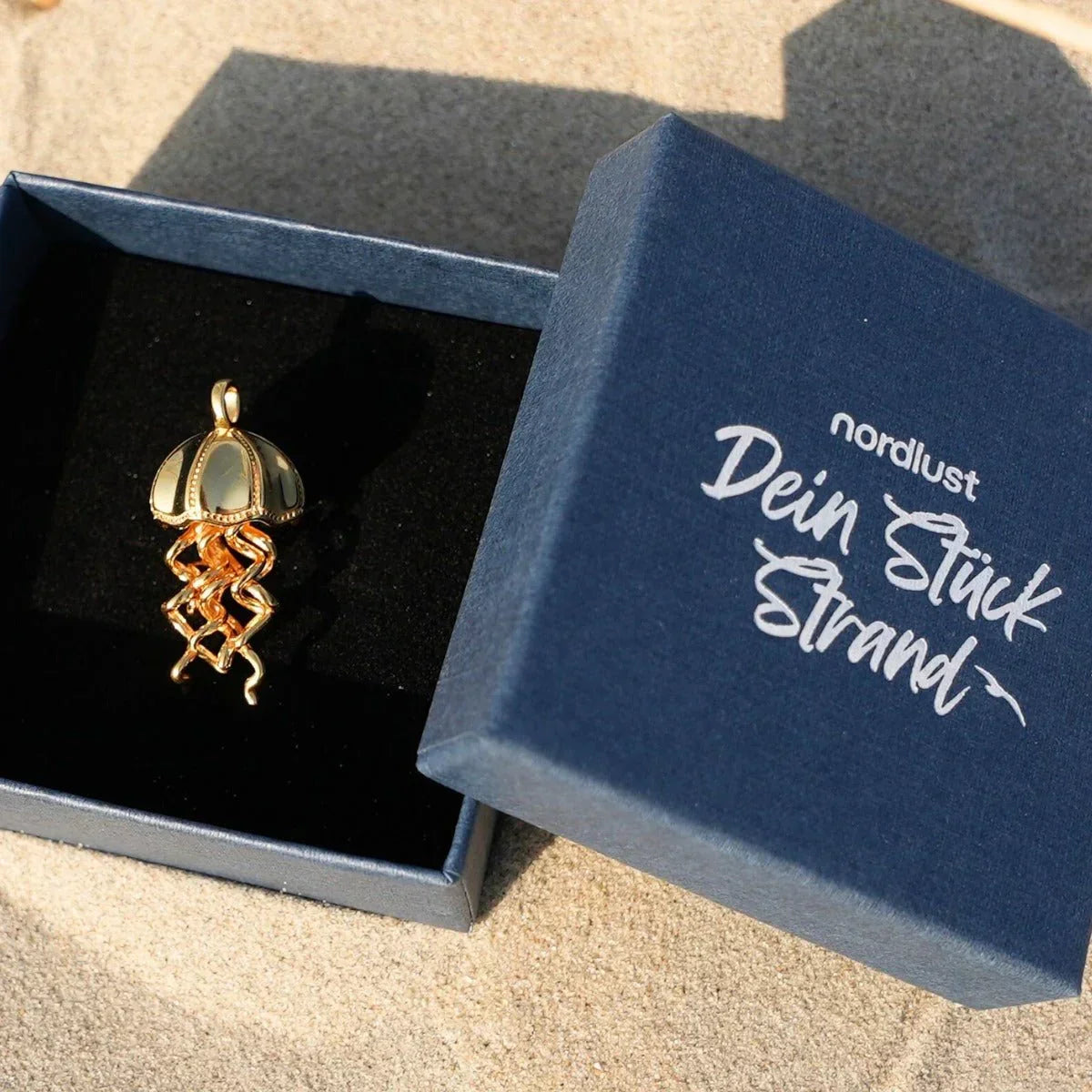 Goldener Quallen-Anhänger maritimer Schmuck in Schmuckschachtel auf Sand