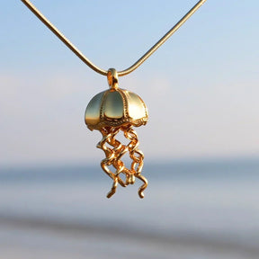 Goldene Qualle Anhänger Kette maritimer Schmuck vor unscharfem Strand Hintergrund