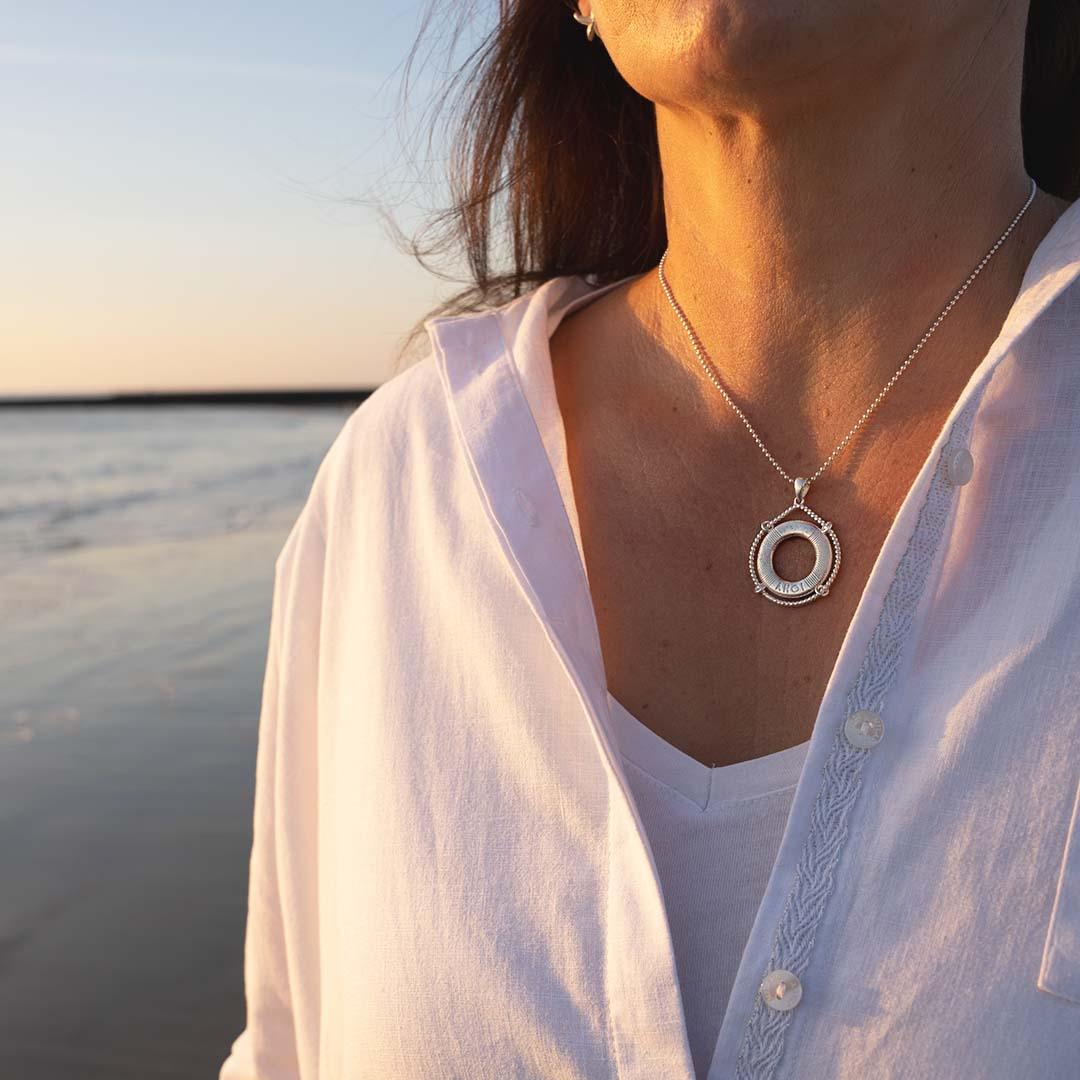 Frau mit silberner Rettungsring-Kette am Strand im Sonnenuntergang, maritimer Schmuck